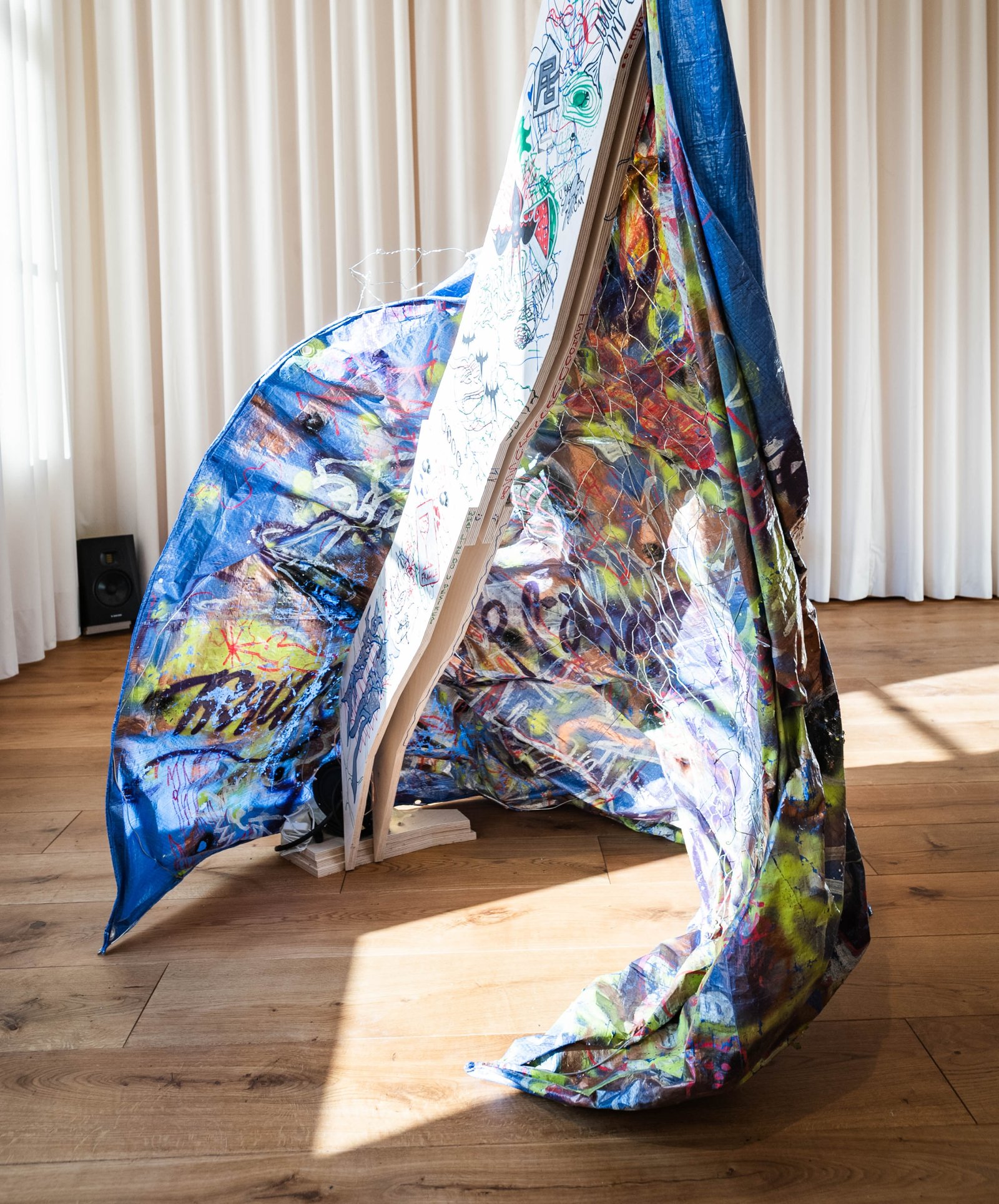 A large colourful woven tent-like sculpture standing in a sunlit room